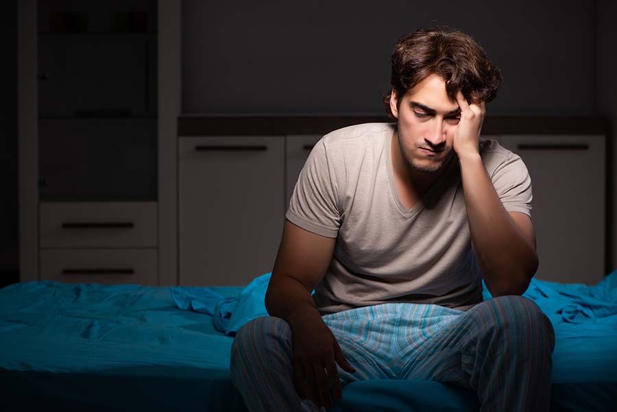 Homem sentado na cama à noite, sem conseguir dormir, com sinais de insônia